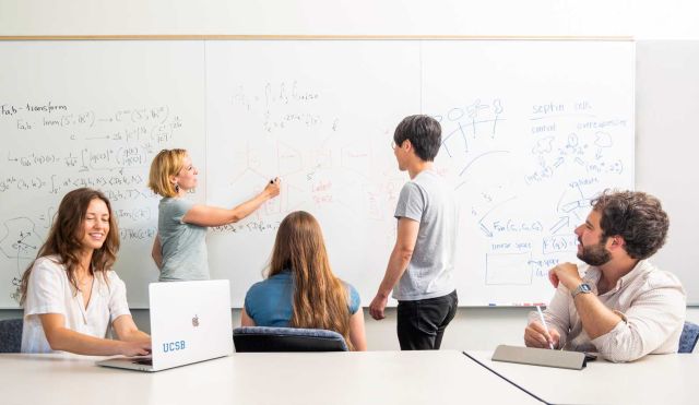 students at table while instructor whiteboards