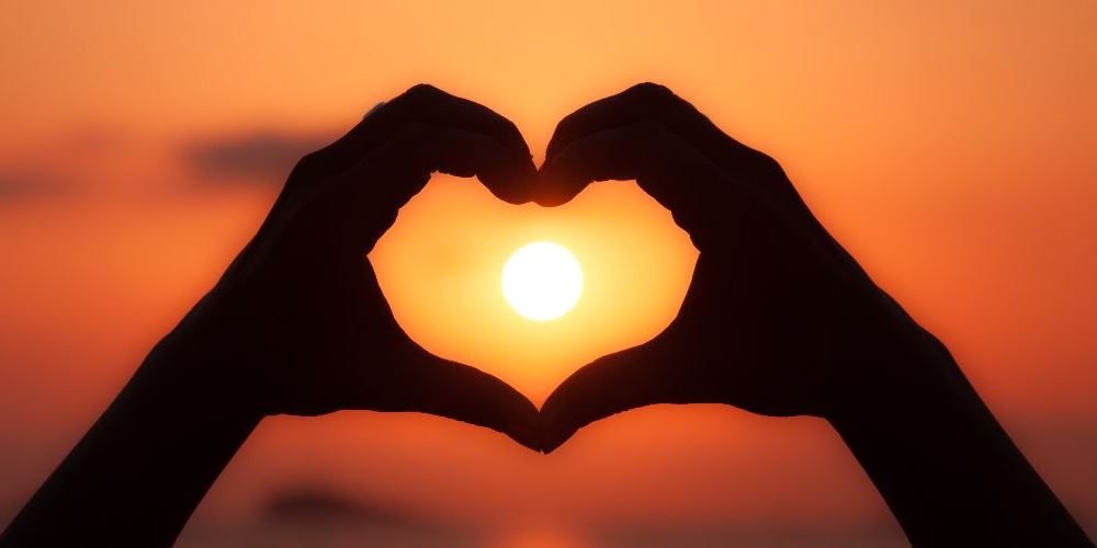 Heart shape, formed by hands, with the setting sun in the middle