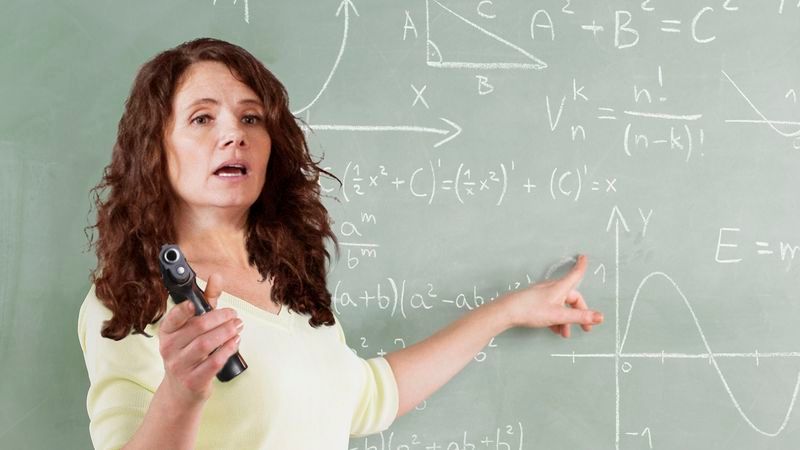 Teacher holding a gun in front of a chalkboard
