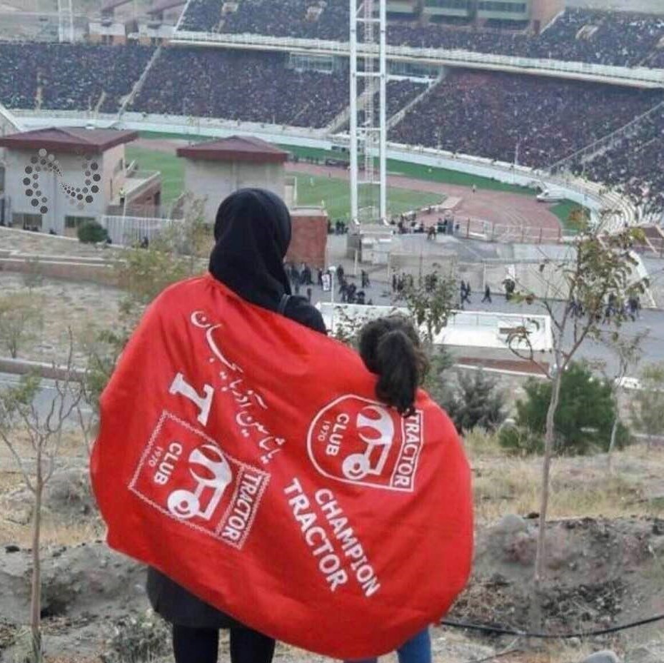 Iranian woman and girl wistfully watch from a nearby hill a soccer match played at a stadium from which they are banned