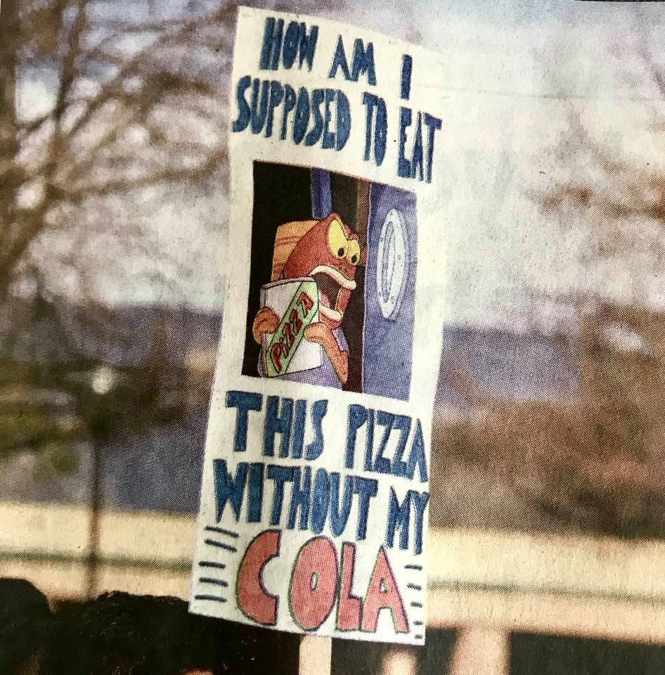 Protest sign reading 'How am I supposed to eat this pizza without my COLA?'