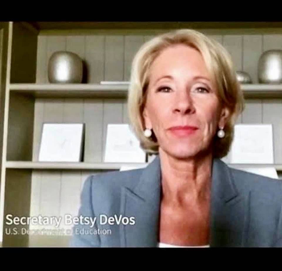US Secretary of Education Betsy DeVos speaking, with the background of a bookcase holding no books