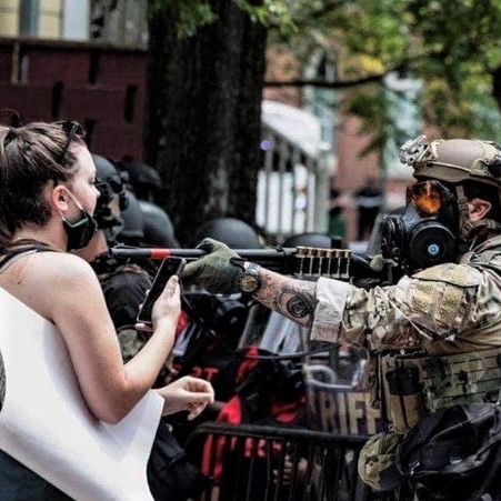 Federal agent aims his rifle at the face of woman protester