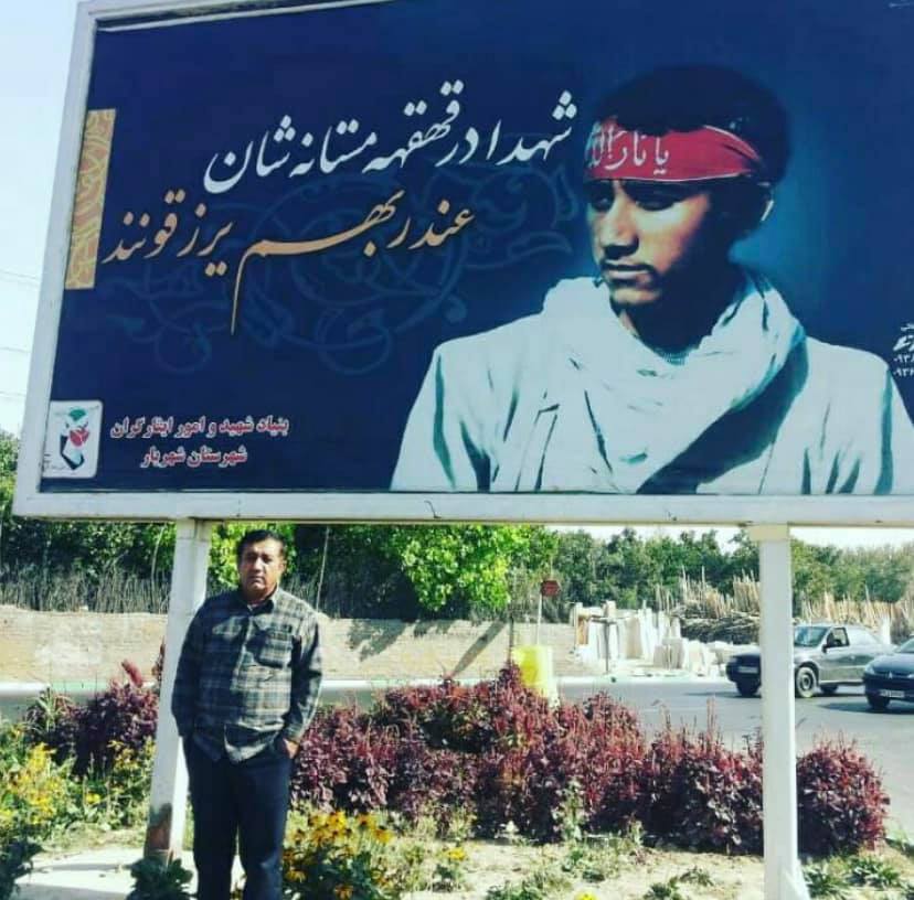 A very alive man, posing in front of a billboard that honors him as a martyr of the Iran-Iraq war