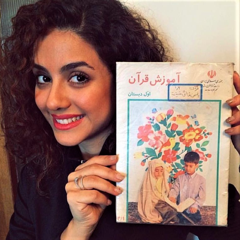 Hijab-less young women shows the cover of an Iranian textbook on which she had appeared with a compulsory hijab