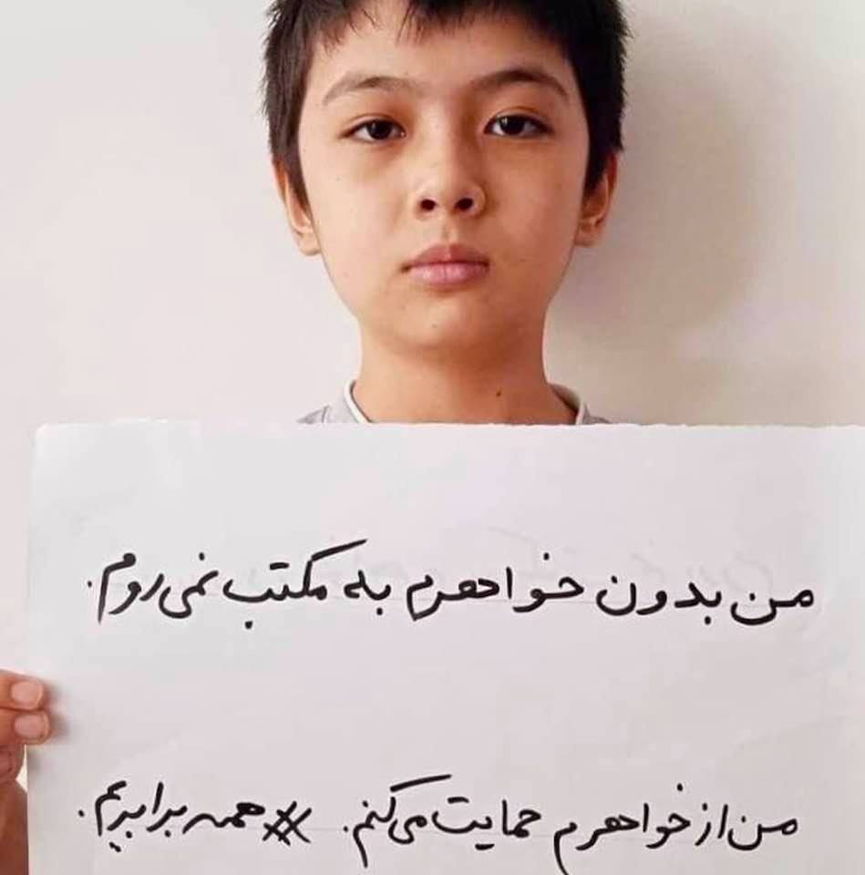 Afghan boy holds a sign that reads: I won't go to school without my sister. I support my sister